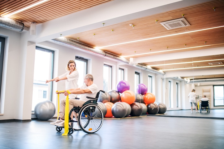 Young attractive woman physiotherapist working with a senior man in wheelchair.